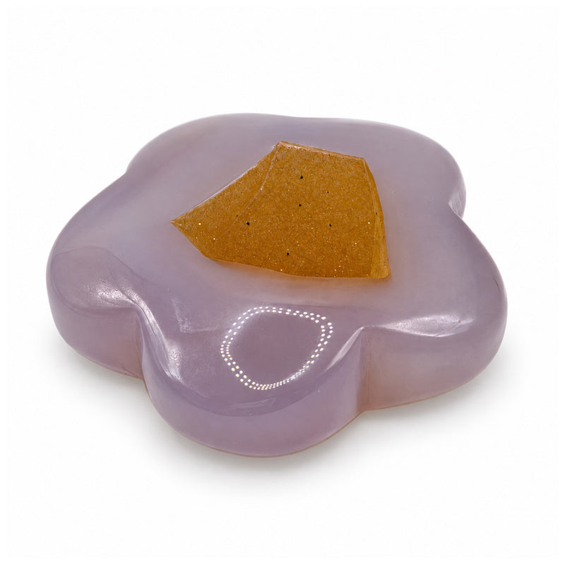 Low angled view of a lavender flower-shaped stone showing its thickness and a large angular amber-colored patch.