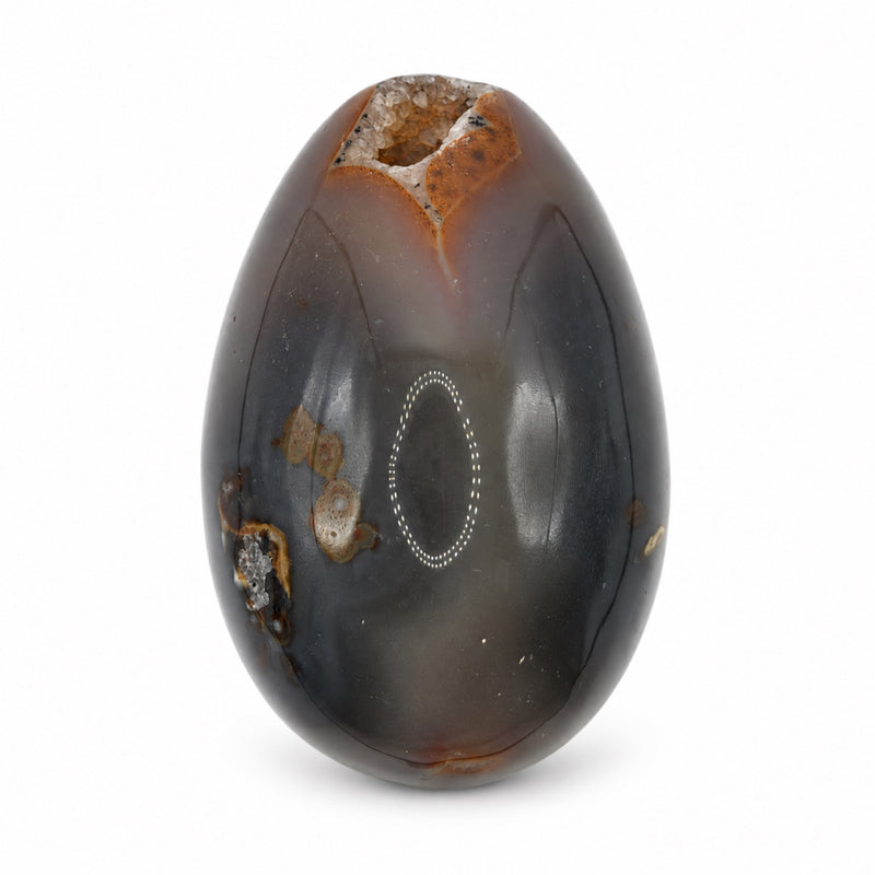 Reverse of a polished gray-brown stone egg with dark curved seams, mineral spots, and a small crystal opening at the top.