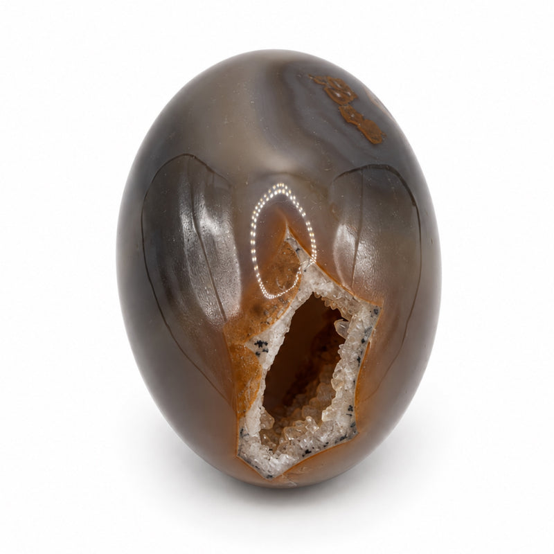 Opposite side of a gray-brown stone egg showing an irregular crystal-lined opening near its lower end.
